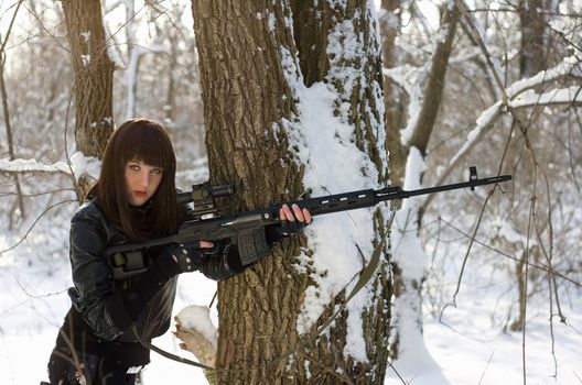 Gorgeous young woman with a sniper rifle near the tree