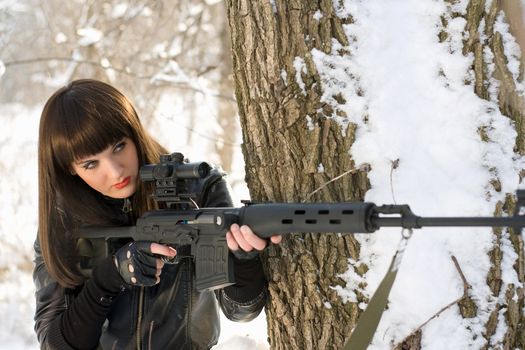Portrait of beautiful young woman with a sniper rifle near the tree