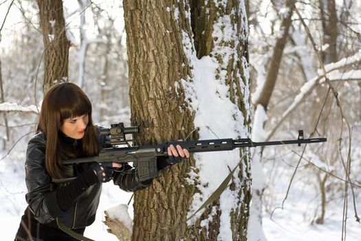 Beautiful young woman with a sniper rifle near the tree