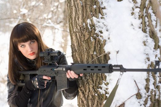 Portrait of young woman with a sniper rifle near the tree