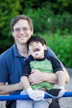 Father holding disabled son at playground
