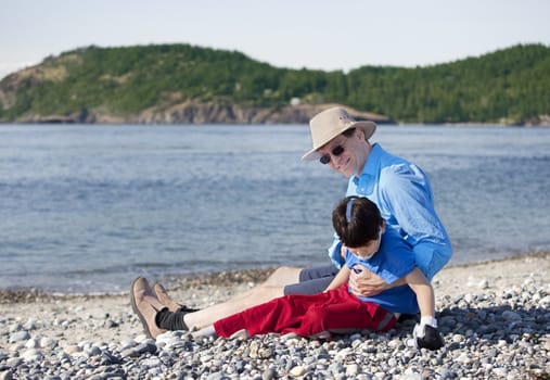 Father sitting on rocky beach playing with disabled son