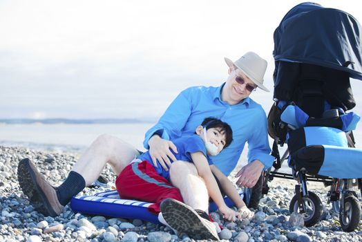 Father sitting on rocky beach playing with disabled son