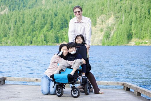 Disabled boy in wheelchair surrounded by family on lake pier