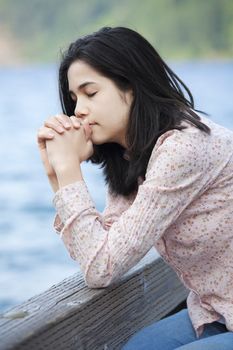 Young teen girl sitting quietly on lake pier, praying