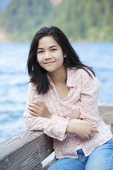 Young biracial teen girl sitting quietly on lake pier, relaxing