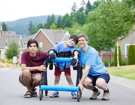 Disabled boy in walker surrounded by father and older brother while walking outdoors on street