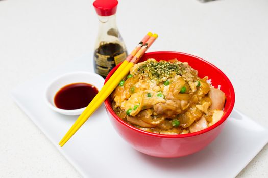 Oyako-don - Japanese checken rice in a red bowl with yellow chopsticks