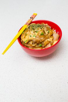 Oyako-don - Japanese checken rice in a red bowl with yellow chopsticks