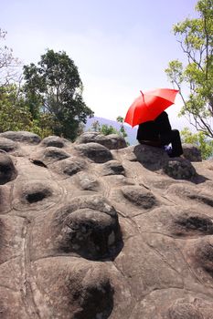 Traveler raise an red umbrella to protect sun light stone on Phu Hin Rong Kla National Park, Phitsanulok in Thailand