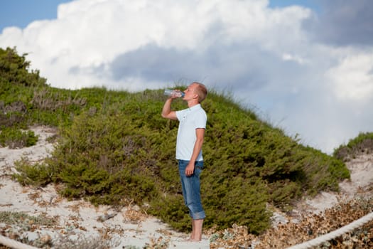 young man ist drinking water summertime dune beach sky background