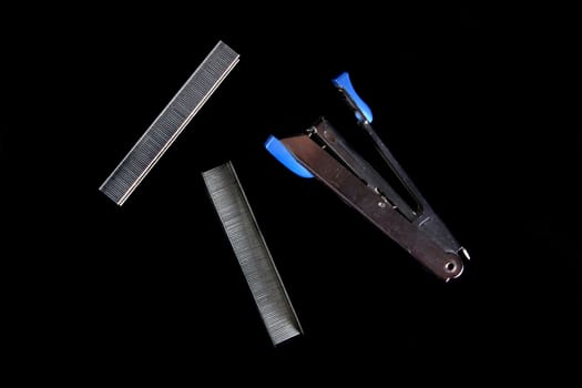 A blue stapler with a set of pins, on black studio background.