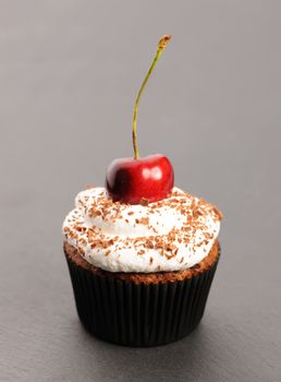 Cupcake with whipped cream and cherry on a table