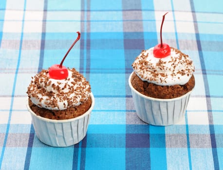 Cupcakes with whipped cream and cherry on a cloth