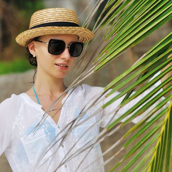 Woman in sunglasses near palm tree wearing hat