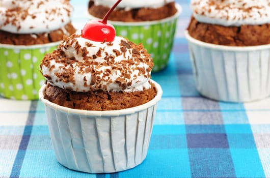 Cupcakes with whipped cream and cherry on a cloth