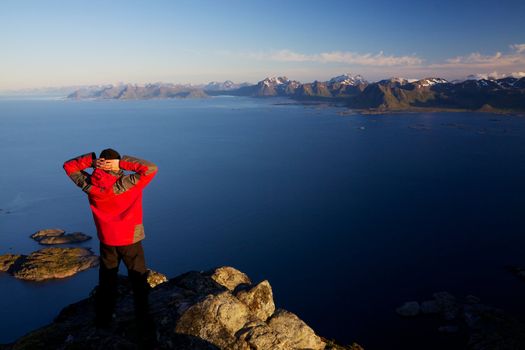 Active man standing on the top of mountain Festvagtinden viewing picturesque scenery of Lofoten islands, Norway