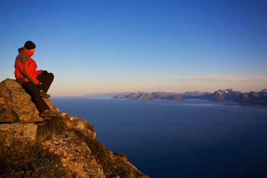 Young man on the top of mountain Festvagtinden with picturesque scenery of Lofoten islands, Norway