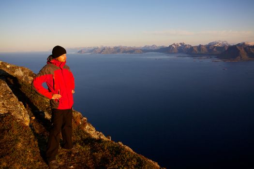 Young man standing on the top of mountain Festvagtinden with picturesque scenery of Lofoten islands, Norway