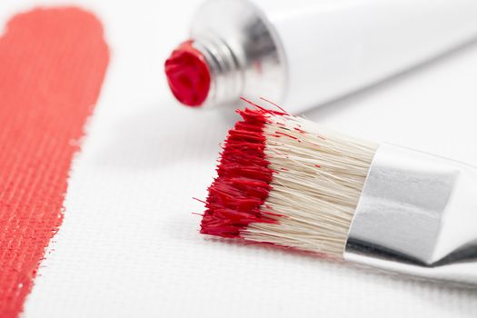 Red paint on paint brush with tube of acrylic paint and paint stroke on canvas