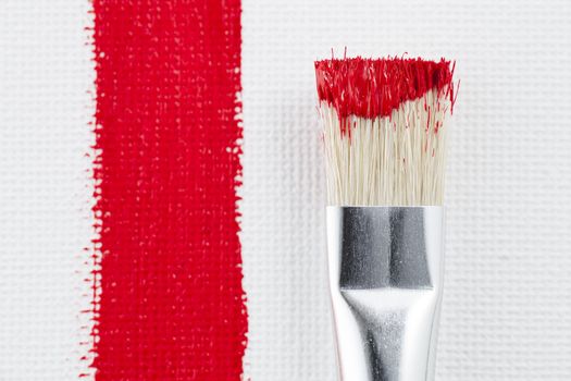 Paint brush with red paint on the end beside red paint stroke on canvas