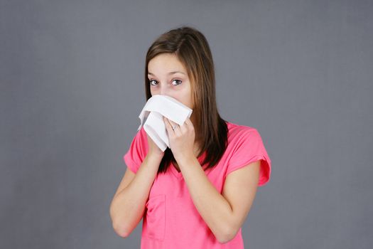 Young woman blowing her nose in a tissue, sick from a cold or flu virus, could be sad or depressed, great for health issues.