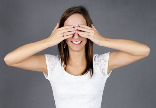 Dressed up young woman with hands on her eyes, smiling, waiting for her big surprise; can be used for wedding proposal, birthday party or others.