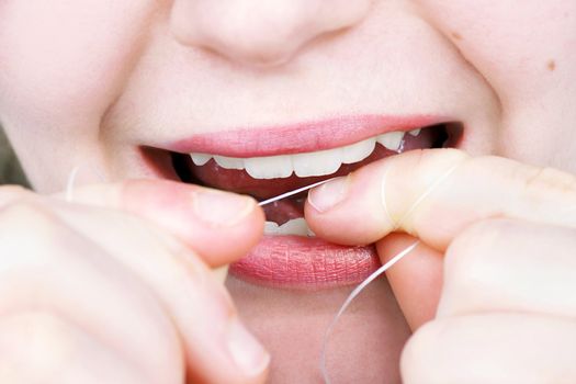 Close up on a young woman flossing her teeth; perfect for dentistry, health and hygiene.