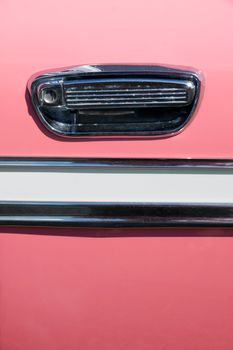 Close up on the handle and chrome decoration on an old pink vintage car; great background.