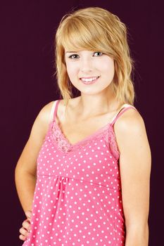 Portrait of cute and innocent yound blond teenager girl smiling, studio shot over deep pink or purple background.