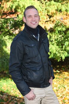 Handsome trendy young man with a cheerful smile standing alone in autumn woodland