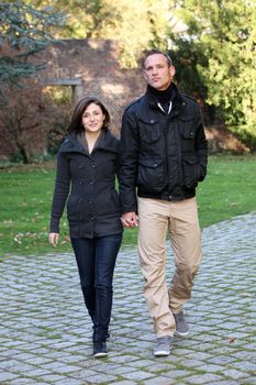 Attractive healthy young couple approaching the camera walking hand in hand along a paved rural walkway Attractive healthy young couple approaching the camera walking hand in hand along a paved walkway