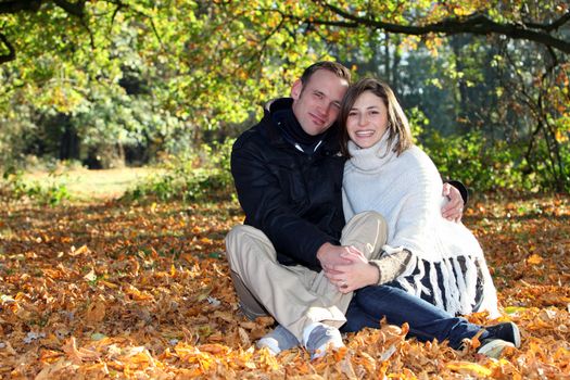 Happy young couple in love sitting in a close embrace amonst autumn leaves in the forest with copyspace
