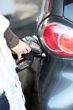 Cropped view of a female hand holding a pump nozzle at a service station as a car is refuelled with petrol or diesel Cropped view of a female hand holding a pump nozzle at a service station as a car being refuelled with petrol or diesel