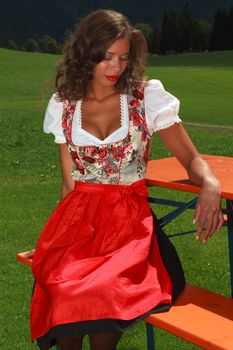 Young beauty in Bavarian dress sitting on a bench dreamy