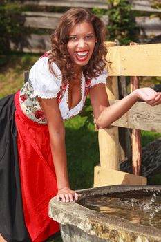 Young beauty in Bavarian costume has fun at the fountain