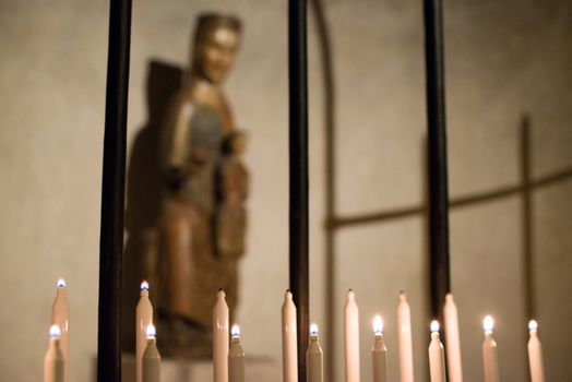 Lit candles in a church, with an an icon of Virgin Mary in the background