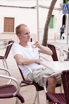 young man sitting outdoor in a cafe in summer drinking water