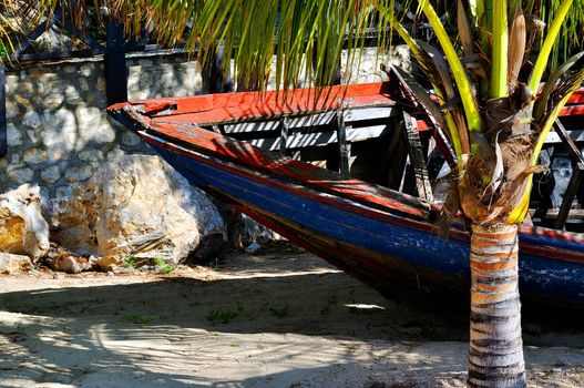 An old and damaged wooden boat lies abandoned near a tropical beach in Haiti.