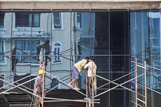 Builders on a scaffolding at work on a high rise block with the reflections showing on glass window surfaces