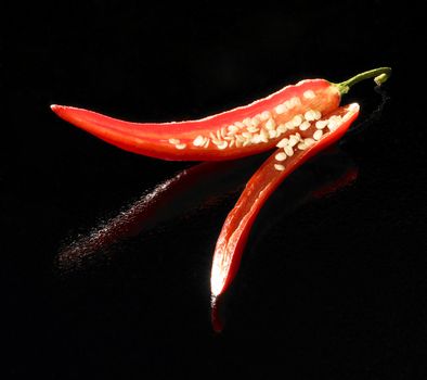 studio shot of a red sliced chili in black reflective back