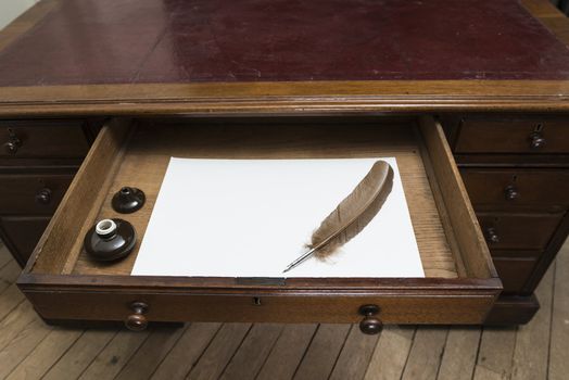 Vintage set with quill and ink pot on top of parchment paper inside writing desk drawer.