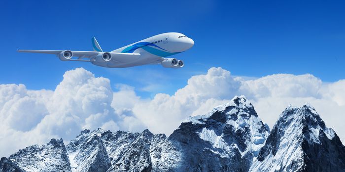 White passenger plane flying in the blue sky above the mountains with snow tops