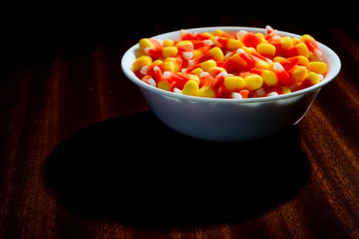 Candy corn in a bowl on a table that is lightly lit.