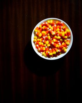 Top down view of candy corn on a dim lit wood table giving a creepy scary vibe
