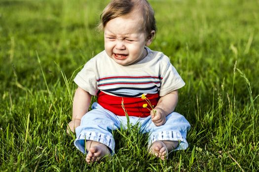 little boy sitting on the grass and weeps