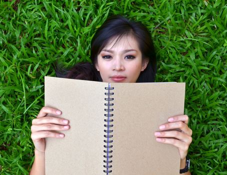 Woman lying on green grass with a book 