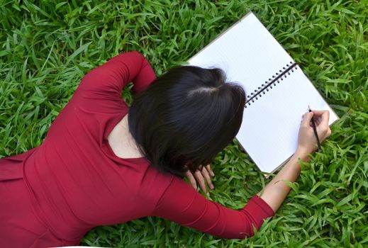 pretty women lying on green grass and writing book