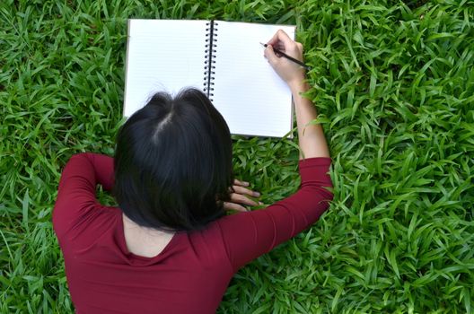 pretty women lying on green grass and writing book