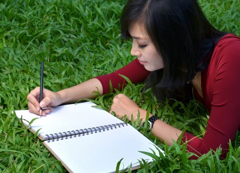 pretty women lying on green grass and writing book